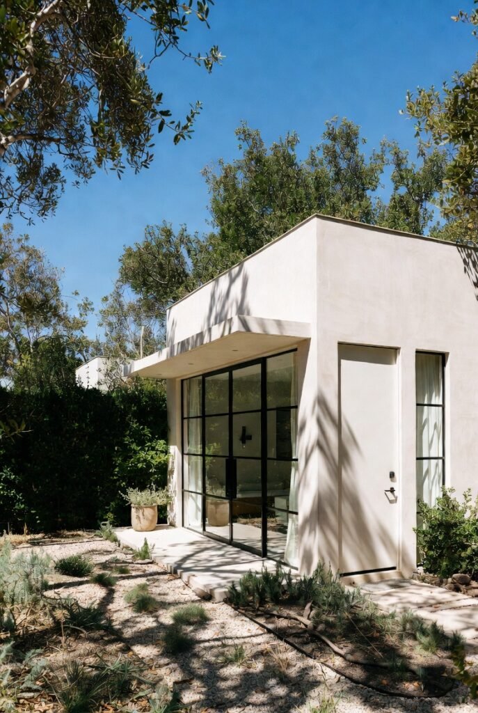 Minimalist Los Angeles ADU featuring light stucco exterior, steel-framed windows, and desert landscaping with natural sunlight and shadows.
