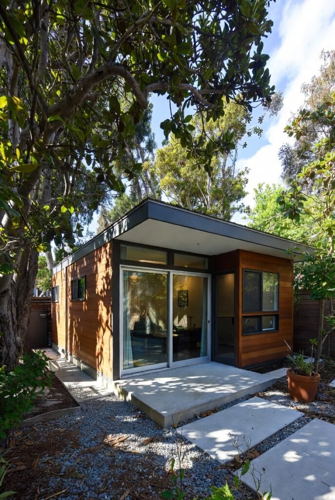 Contemporary ADU in Los Angeles featuring warm wood siding, flat roof, and sliding glass doors surrounded by lush trees.